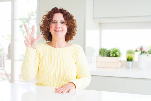 Mulher sênior bonita vestindo suéter amarelo mostrando e apontando para cima com os dedos número três, sorrindo confiante e feliz
. - Foto, Imagem