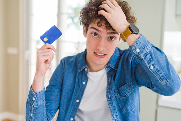 Νεαρός άνδρας κρατά πιστωτική κάρτα τόνισε με το χέρι στο κεφάλι, σοκαρισμένος με ντροπή και έκπληξη πρόσωπο, θυμωμένος και απογοητευμένος. Φόβο και αναστάτωση για το λάθος. - Φωτογραφία, εικόνα