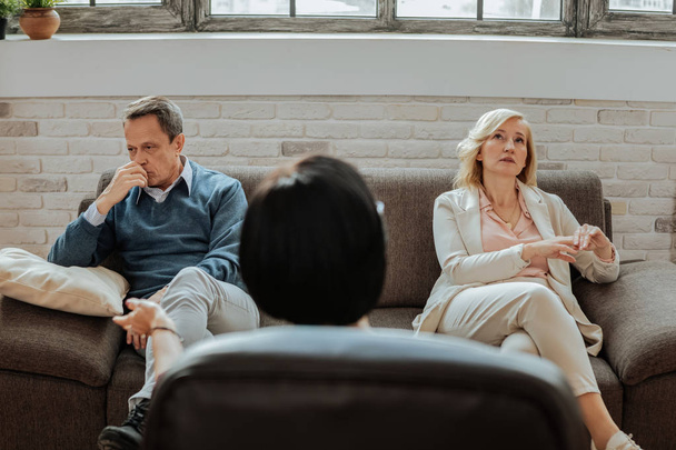 Confused and upset adult couple sitting on different sides of couch - Foto, imagen