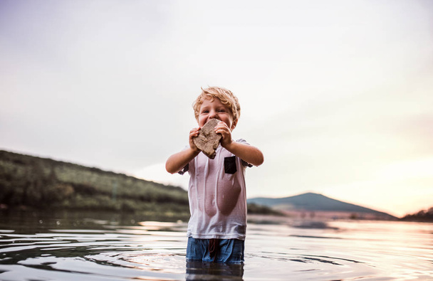 A small toddler boy playing outdoors by the river in summer. - Fotó, kép