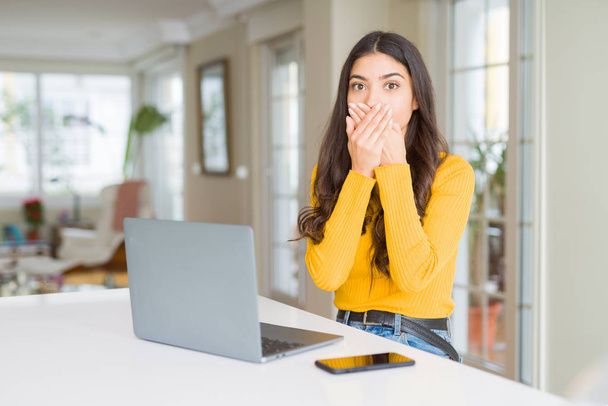 Young woman using computer laptop shocked covering mouth with hands for mistake. Secret concept. - Фото, изображение