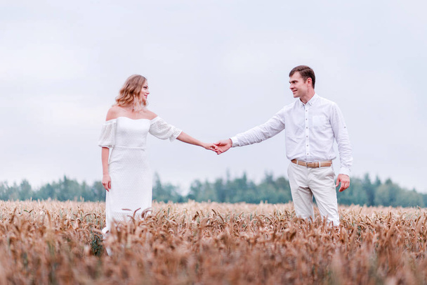 Nevěsta a ženich, drželi se za ruce na pozadí pšeničné pole - Fotografie, Obrázek