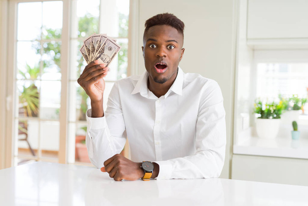 Hombre afroamericano sosteniendo billetes de cincuenta dólares asustado en shock con una cara sorpresa, asustado y emocionado con la expresión del miedo
 - Foto, Imagen