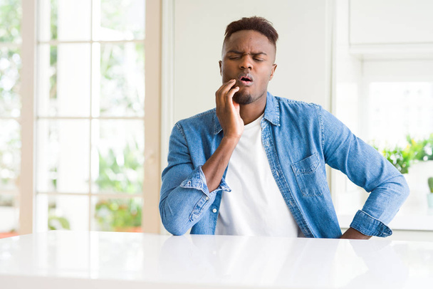 Knappe Afro-Amerikaanse man thuis raken mond met de hand met pijnlijke expressie vanwege kiespijn of tandheelkundige ziekte op tanden. Tandarts concept. - Foto, afbeelding