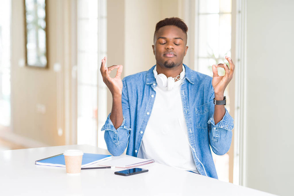 Африканский американец, учащийся с помощью ноутбуков и наушников, расслабляется и улыбается с закрытыми глазами, делая жест медитации пальцами. Концепция йоги
. - Фото, изображение
