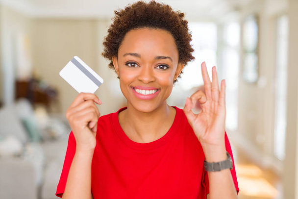 Молодая африканская американка держит кредитную карту делает хорошо знак с пальцами, отличный символ
 - Фото, изображение
