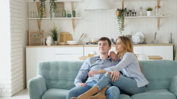 couple sits on cosy blue sofa watching TV in modern kitchen - Кадры, видео