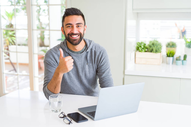 Красивый латиноамериканец работает с компьютером ноутбук счастлив с большой улыбкой делает хорошо знак, палец вверх пальцами, отличный знак
 - Фото, изображение