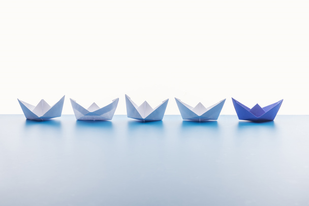 Бумажные лодки на светло-голубой поверхности на белом фоне
 - Фото, изображение