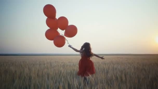 onnellinen nuori tyttö ilmapalloineen juoksee vehnäpellolla auringonlaskun aikaan. 4k-video
. - Materiaali, video