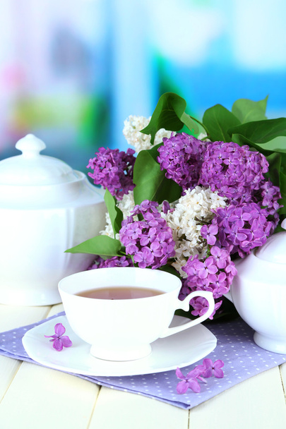 Composition with beautiful lilac flowers, tea service on wooden table on bright background - Photo, image