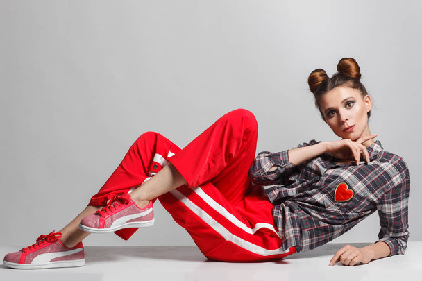 A picture of a fun, positive model wearing a plaid shirt, red sweatpants and sneakers. Studio photo session - Фото, зображення