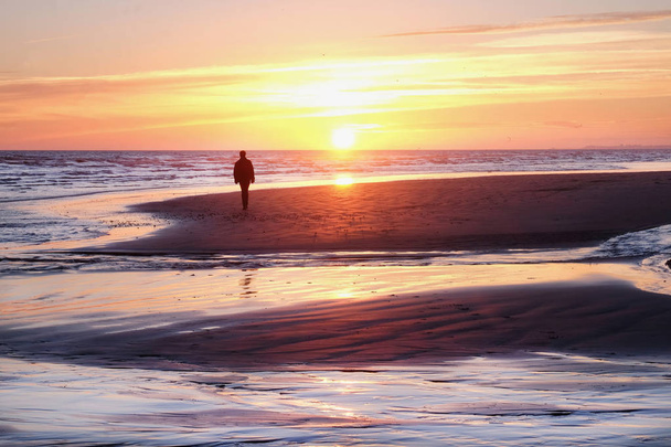 αγνώριστο άτομο που περπατάει σε μια έρημο παραλία στο ηλιοβασίλεμα - Φωτογραφία, εικόνα