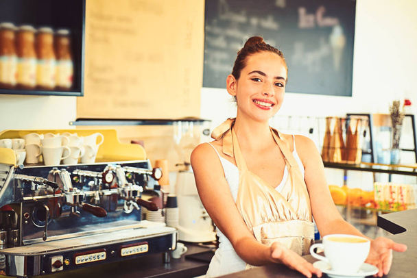 One of lifes great pleasures. Brewing coffee in coffeehouse. Barista serve cup of hot coffee drink with smile. Woman barista in coffee shop. Pretty woman stand behind cafe counter - Photo, Image