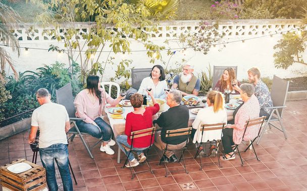 幸せな家族は夕食バーベキュー屋外で赤ワインを食べ、飲む-バーベキューパーティーで一緒に楽しい食事をしている異なる年齢の人々 -食べ物、両親、週末の活動 - 写真・画像