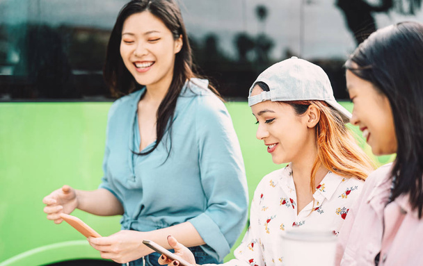 Chicas asiáticas felices usando el teléfono móvil al aire libre - Gente joven millennial divirtiéndose con la nueva tecnología de aplicaciones para teléfonos inteligentes fuera - Concepto de amistad, tecnología y estilo de vida adolescente
 - Foto, imagen