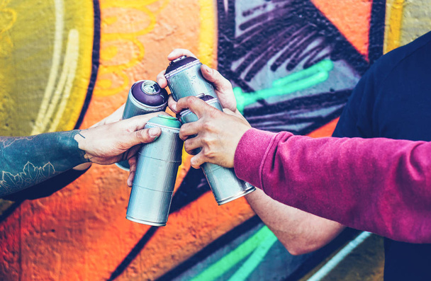 Groep graffitikunstenaars stapelen handen terwijl spray kleur tegen muurschildering achtergrond - jonge schilder op het werk - Concept van hedendaagse kunst, straatkunst en mensen jeugd levensstijl kunnen - Foto, afbeelding