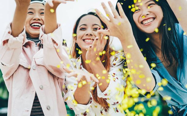 Happy Asian friends having fun throwing confetti outdoor - Young trendy people celebrating at festival event outside - Party, entertainment and youth holidays lifestyle concept - Foto, Bild