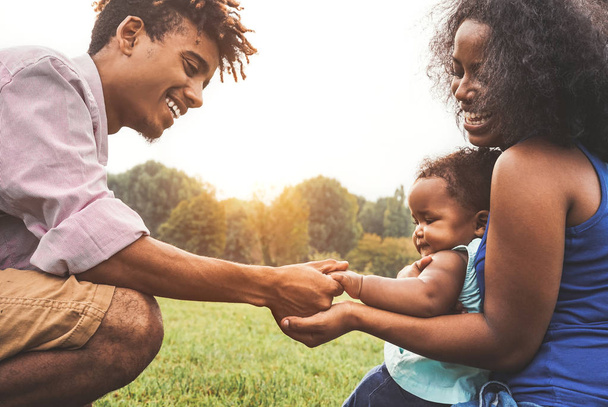 Счастливая африканская семья, проводящая время вместе в общественном парке - мать и отец весело играют со своей дочерью на открытом воздухе на закате - Любовь, родители и концепция счастья
 - Фото, изображение