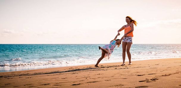 Щаслива мати і дочка розважаються на тропічному пляжі на заході сонця - Сім'я грає наступне море під час літніх канікул - Концепція батьків, кохання і щастя
 - Фото, зображення