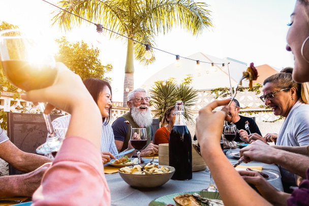 Happy family doing a dinner during sunset time outdoor - Groupe d'amis divers qui s'amusent à dîner ensemble à l'extérieur - Concept de style de vie personnes, nourriture et activités de week-end
 - Photo, image