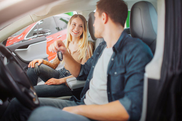 Young family buying first electric car in the showroom. Attractive smiling couple talking and sitting in the cabin of modern electric hybrid vehicle before test driving. Electric car sale concept - Foto, afbeelding