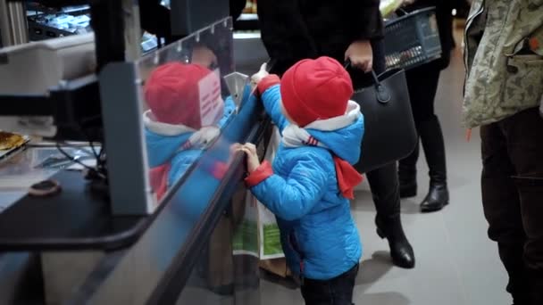 Egy 3 éves gyerek mellett a szupermarket pénztáros áll és nézi az áruk. - Felvétel, videó