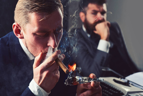 Waste of money. Man light up cigar from dollar banknote. Rich man smoking during business meeting. Businessmen have money to burn. Business partners writing financial report. Filthy with money - Foto, Bild