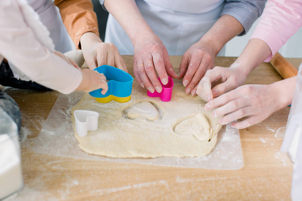 Two sisters, grandmother and little baby daughter are cooking in the kitchen to Mothers day, lifestyle photo series in bright home interior. Hands cutting hearts cookies from dough fom mother's day - Фото, изображение