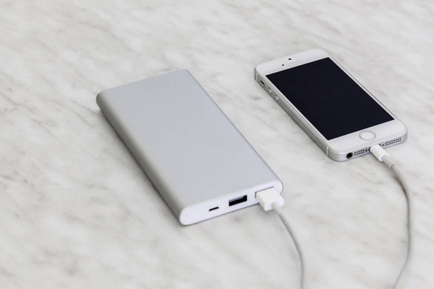 iPhone SE charging with power bank on marble background - Foto, afbeelding