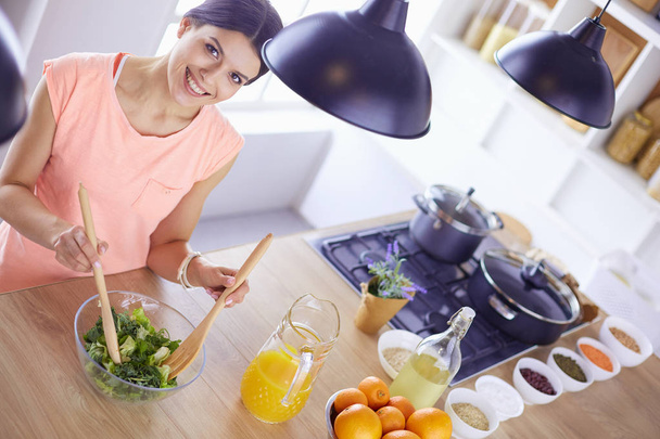 Gülümseyen genç kadın mutfakta taze salata karıştırıyor.. - Fotoğraf, Görsel