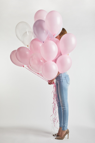 girl in high heels and denim covering face with pink air balloons on white - 写真・画像