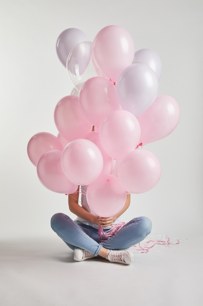 Mädchen sitzt und bedeckt Gesicht mit rosa Luftballons auf weißem Grund - Foto, Bild
