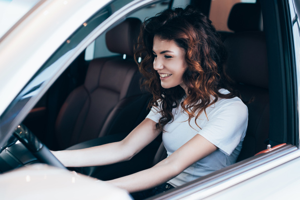 selective focus of cheerful curly woman sitting in automobile  - Fotografie, Obrázek