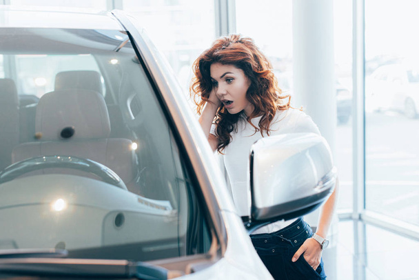 selective focus of shocked curly woman standing with hand in pocket near automobile  - Foto, Imagem