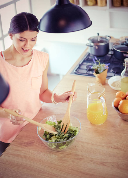 Mosolygó fiatal nő keverés friss saláta a konyhában. - Fotó, kép