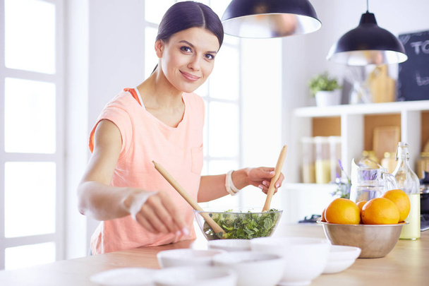 Χαμογελαστή νεαρή γυναίκα ανακατεύοντας φρέσκια σαλάτα στην κουζίνα. - Φωτογραφία, εικόνα