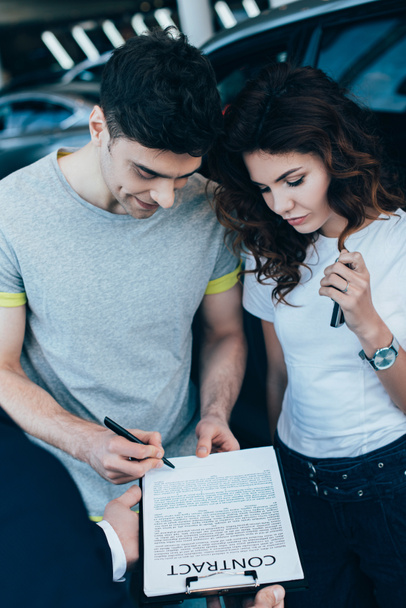 vista aerea di rivenditore di auto in possesso di appunti mentre l'uomo felice firma contratto vicino attraente donna riccia
   - Foto, immagini
