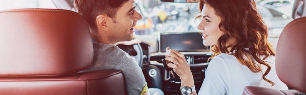 panoramic shot of happy woman and handsome man looking at each other while sitting in automobile  - Foto, Imagem