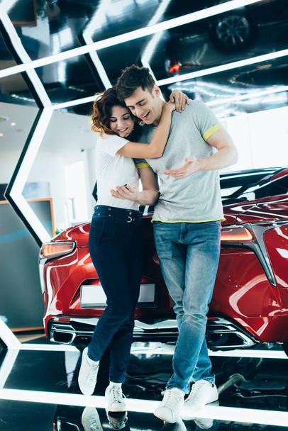 cheerful curly woman hugging man while standing near automobile  - Foto, immagini