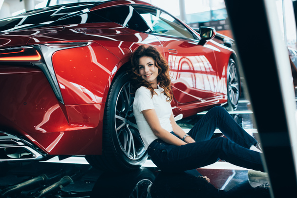 selective focus of happy woman sitting near new luxurious car in car showroom - 写真・画像