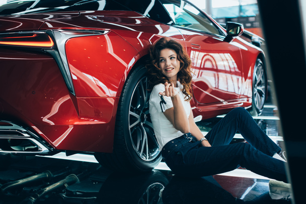 selective focus of happy woman sitting on floor near new luxurious car - Photo, Image