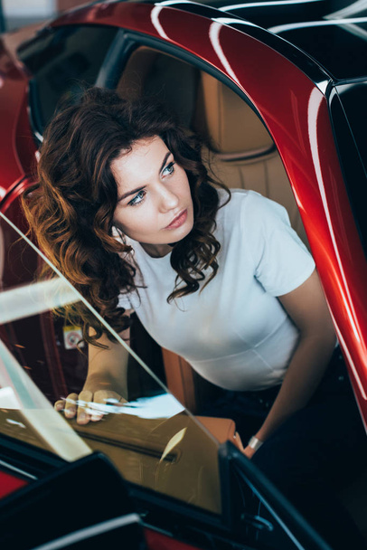 selective focus of pretty woman sitting in new red car - Zdjęcie, obraz