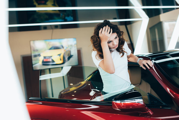 selective focus of exhausted woman standing new car in car showroom - Fotografie, Obrázek