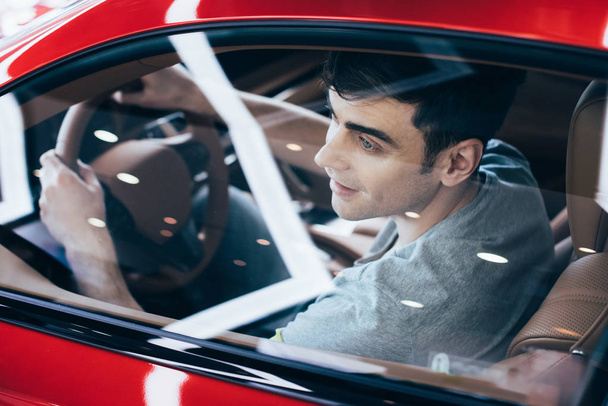 selective focus of smiling man sitting at steering wheel in new car - Photo, image