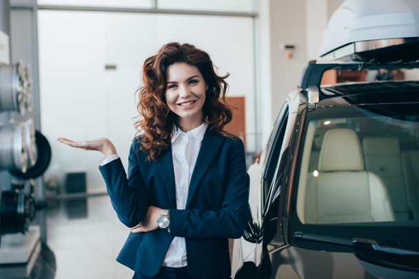pretty businesswoman standing new car in car showroom and looking at camera - Photo, Image