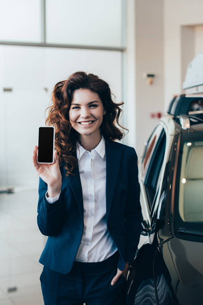 smiling businesswoman holding smartphone with blank screen and looking at camera - Photo, Image