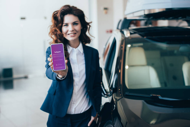 selective focus of smiling businesswoman holding smartphone with instagram app on screen  - Fotó, kép