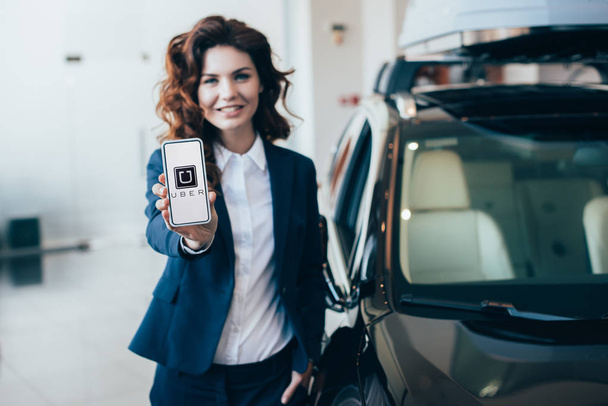selective focus of pretty businesswoman holding smartphone with uber app on screen  - Fotografie, Obrázek