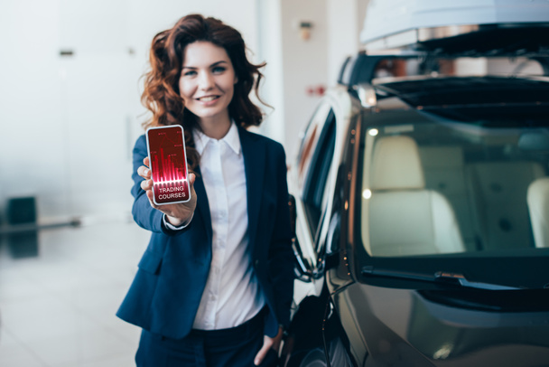 Selektywny fokus businesswoman posiadania smartphone z kursów handlowych aplikacji na ekranie i trzyma rękę w kieszeni - Zdjęcie, obraz